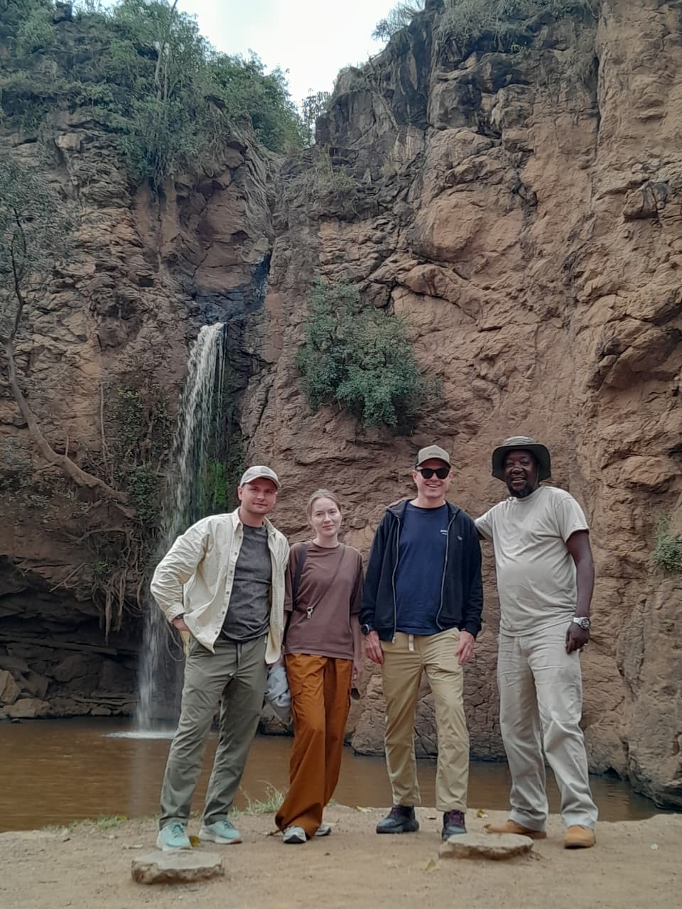 Safari guests and their guide beside a waterfall surrounded by rocky cliffs